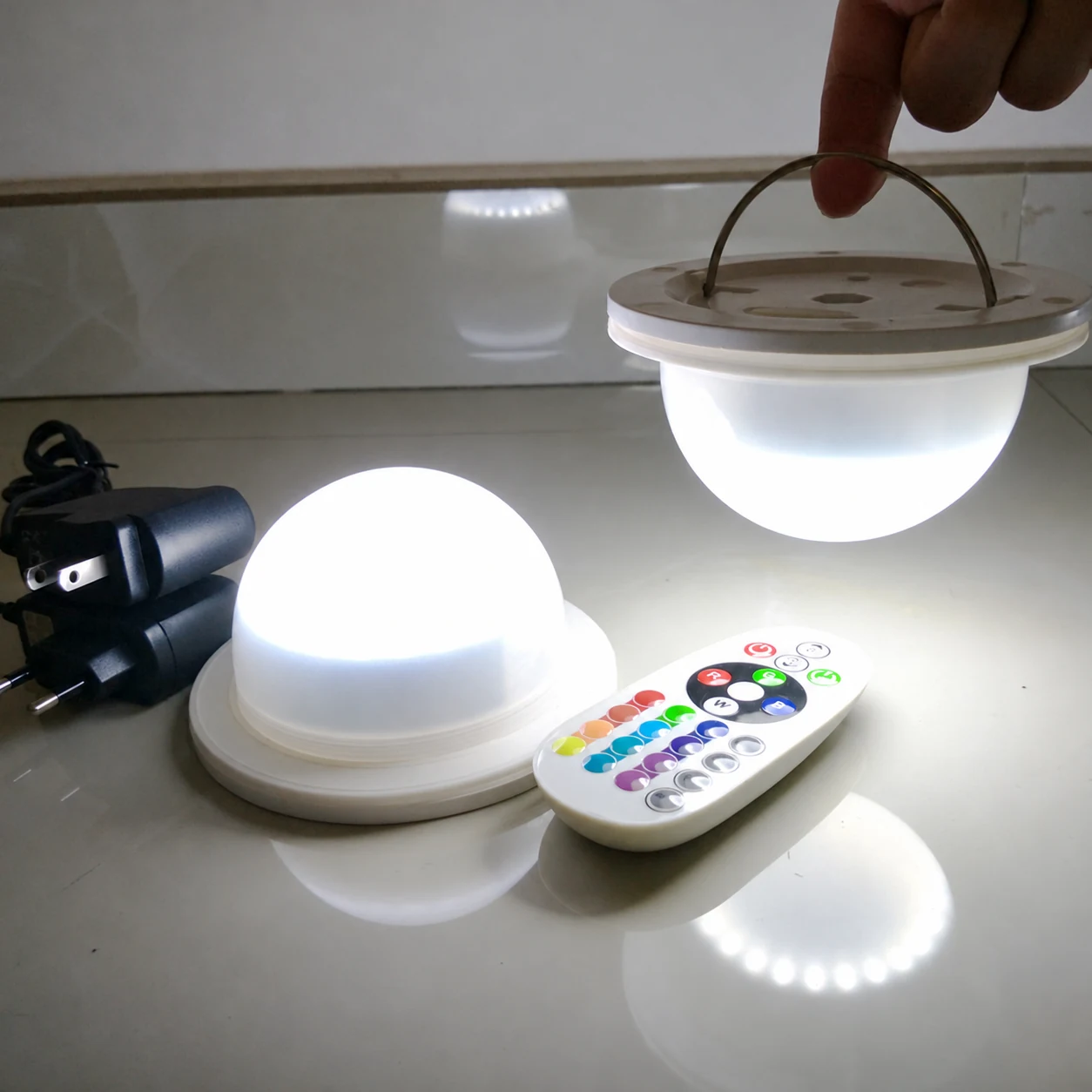 Two Vcan LED modules operating in white light, one held by its handle, with a remote control and power adapters