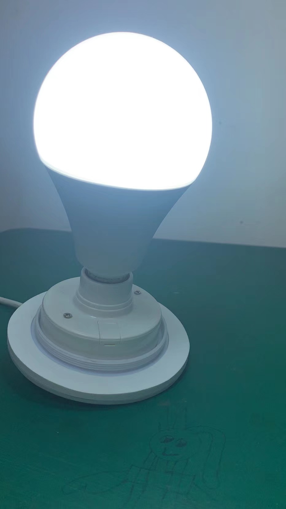 White E27 bulb illuminated during a factory test of the wired light base