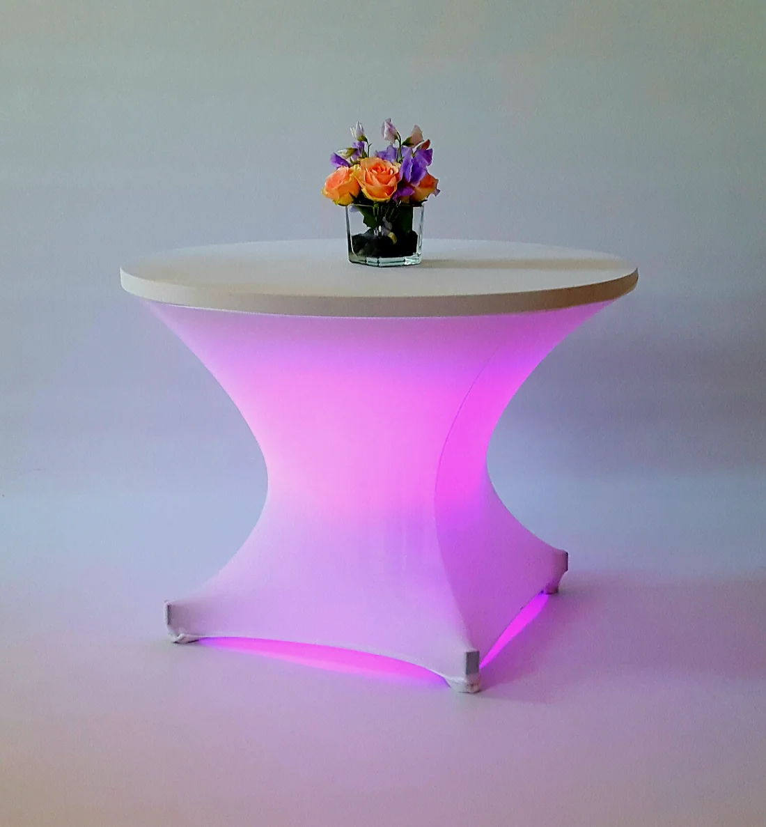 White fabric-covered cocktail table illuminated pink-purple from inside, with a flower arrangement on the tabletop