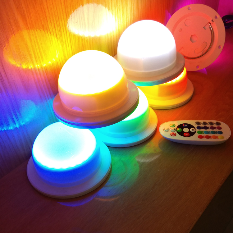 Several real Vcan LED modules displaying white and coloured light beside a handheld remote